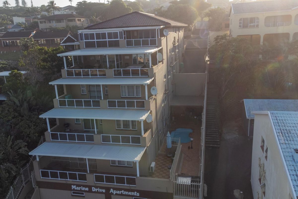 Aerial view of a multi-story apartment complex featuring private balconies, a ground-level swimming pool, and paved outdoor areas.