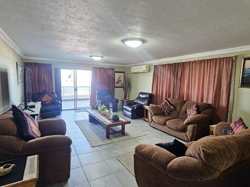 Spacious living room featuring tiled flooring, crown molding, wall-mounted air conditioning unit, and sliding glass doors leading to an outdoor balcony.