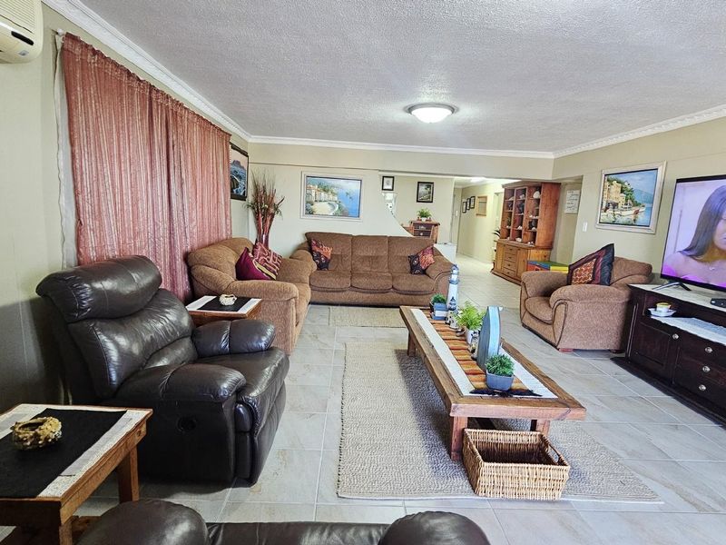 Spacious open-plan living area featuring tiled flooring, crown molding, and a wall-mounted air conditioning unit.