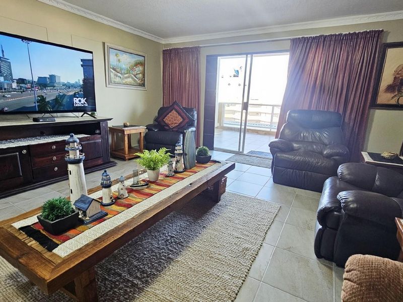 A comfortable living room featuring tiled flooring, crown molding, and sliding glass doors that provide access to an outdoor balcony area.