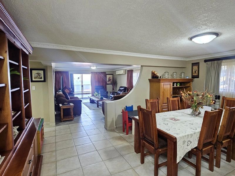 Spacious open-plan living and dining area featuring tiled flooring, decorative crown molding, and a semi-partitioned layout leading to a balcony.