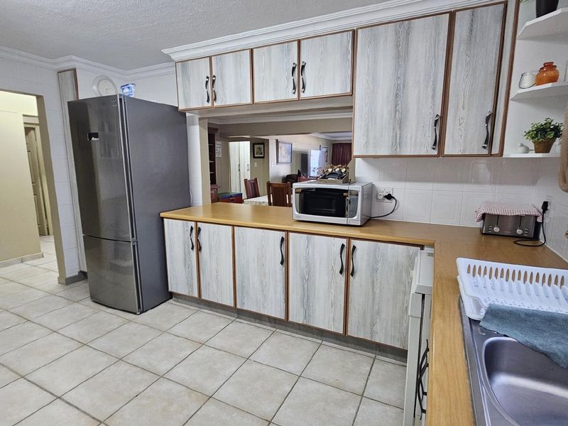 A functional kitchen featuring wood-look cabinetry, laminate countertops, tiled flooring, and a pass-through window connecting to the adjacent living area.