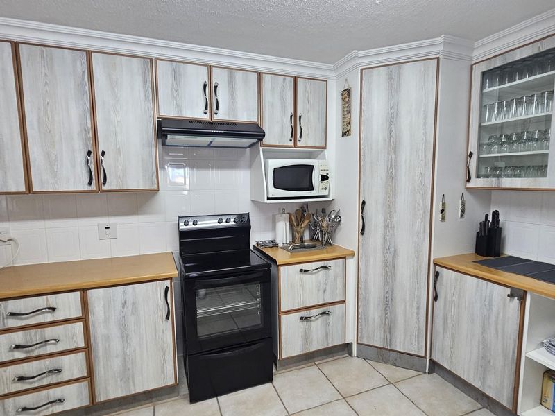 A functional kitchen featuring wood-grain cabinetry, tiled backsplash, built-in oven with extractor fan, and tiled flooring.