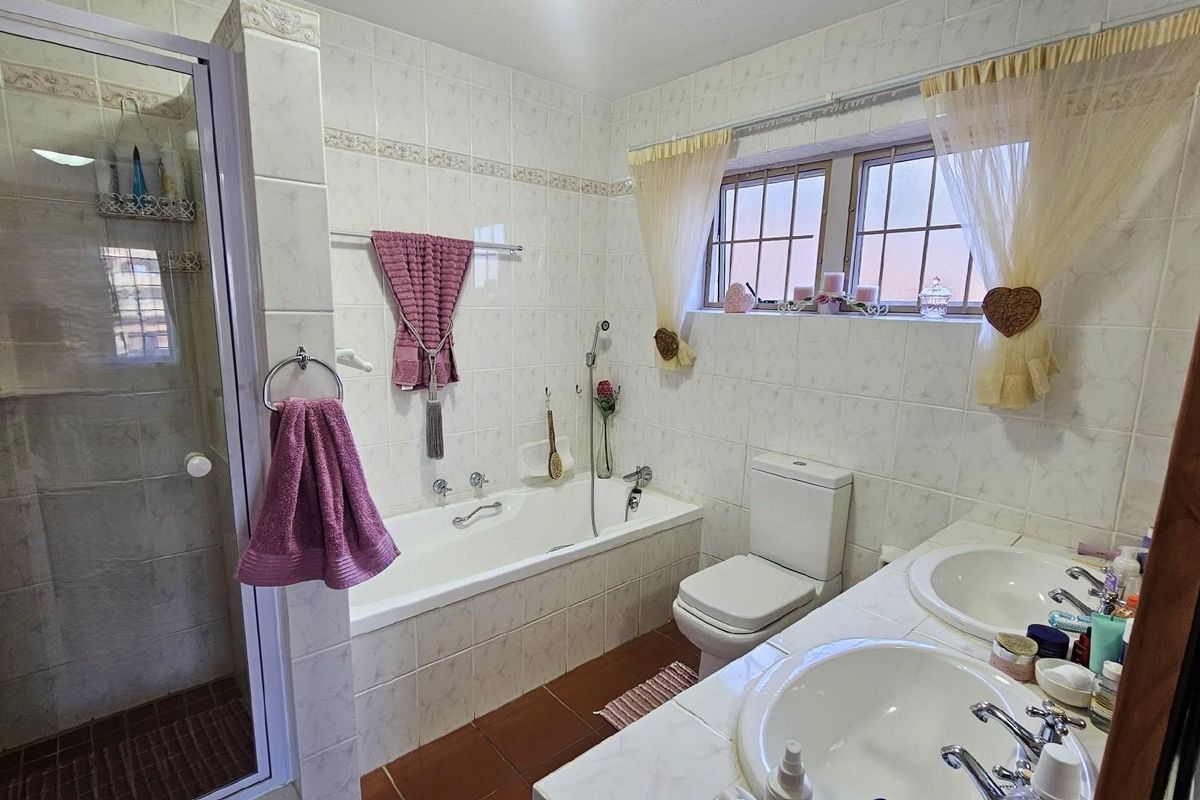 A functional bathroom featuring a built-in bathtub, separate glass-enclosed shower, dual vanity basins, and a toilet with tiled walls and flooring.
