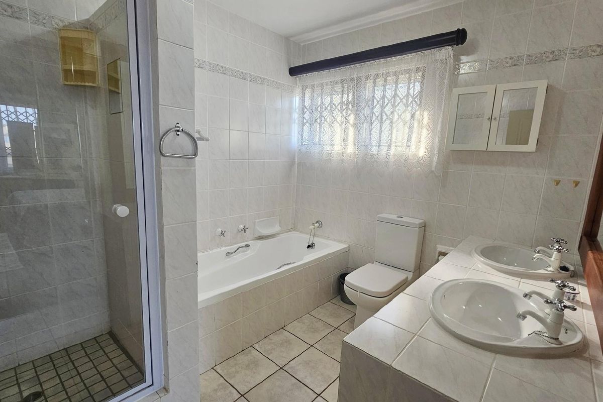 A functional bathroom featuring a separate shower, bathtub, and a double vanity with tiled countertops and white wall tiling.