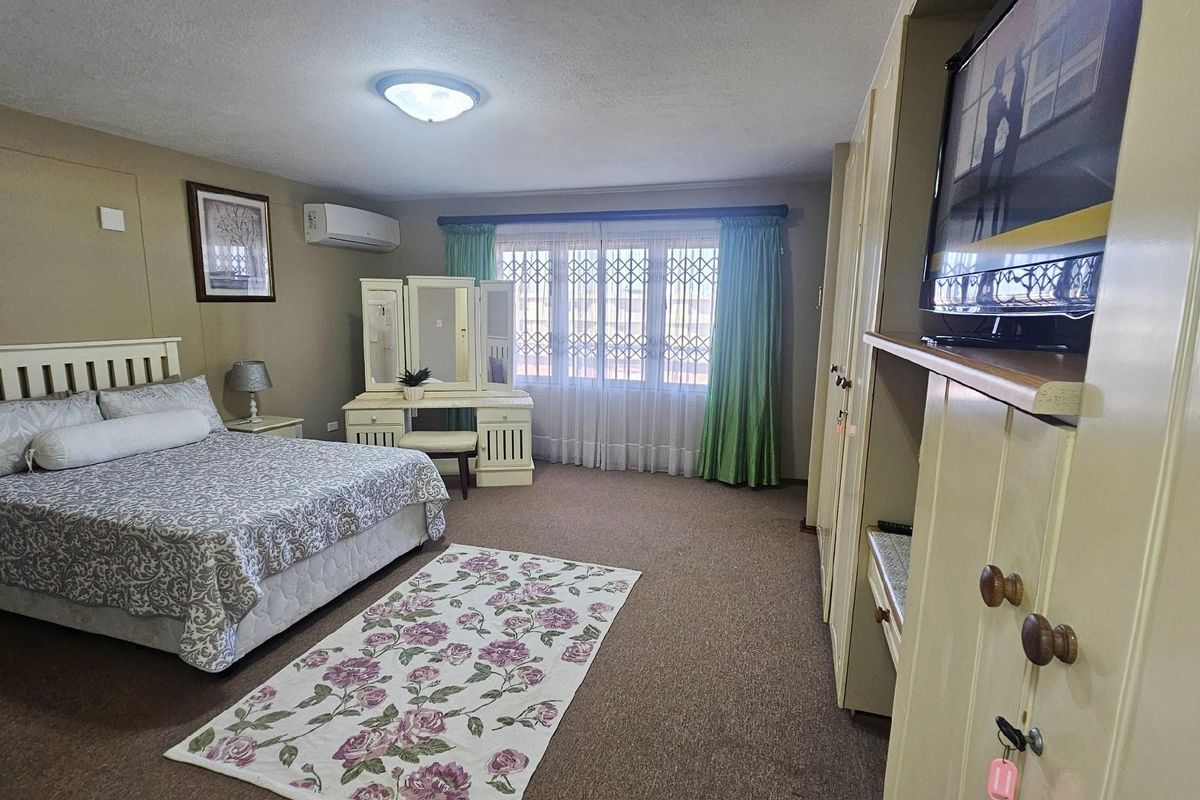 Spacious bedroom featuring built-in cupboards, wall-mounted air conditioning unit, and security gates on the windows.