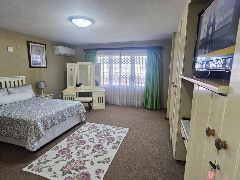 Spacious bedroom featuring built-in cupboards, wall-mounted air conditioning unit, and security gates on the windows.