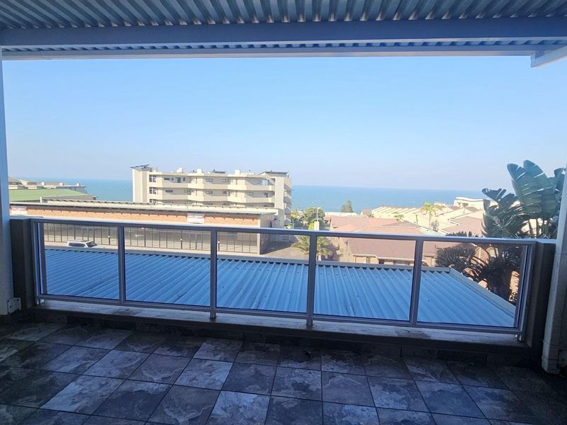 Covered balcony featuring tiled flooring and a glass balustrade, offering expansive views of the surrounding neighborhood and the ocean.