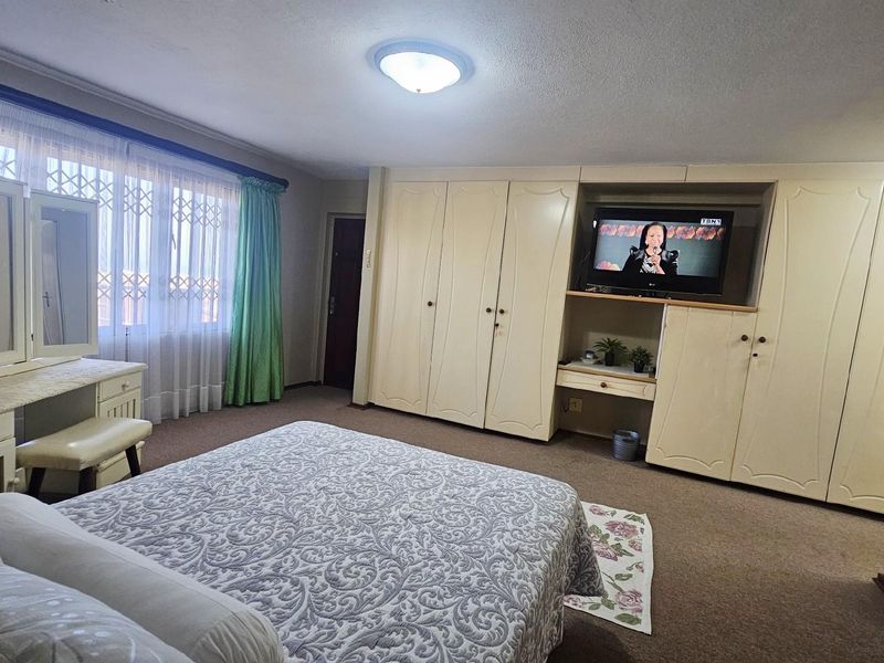 Spacious bedroom featuring extensive built-in cabinetry, carpeted flooring, and large windows with security gates, offering ample storage and natural light.