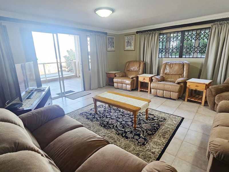 A spacious living room featuring tiled flooring, crown molding, and large sliding glass doors providing access to an outdoor patio area.