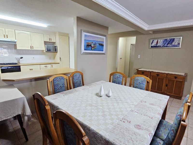 Open plan dining area adjacent to a functional kitchen with built-in cabinetry, tiled flooring, and decorative ceiling cornices.