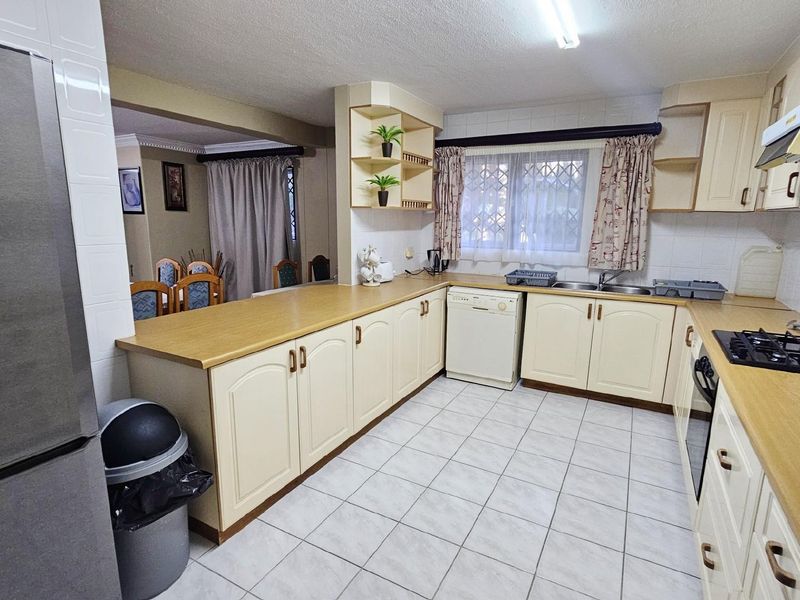 A functional kitchen featuring light-toned cabinetry, laminate countertops, a built-in gas hob, and tiled flooring, with an open-plan layout connecting to the dining area.