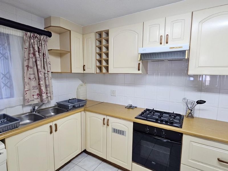 A functional kitchen featuring cream-colored cabinetry, a built-in oven, gas hob, extractor fan, and a double-basin sink with tiled splashbacks.