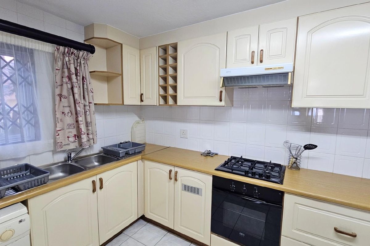 A functional kitchen featuring cream-colored cabinetry, a built-in oven, gas hob, extractor fan, and a double-basin sink with tiled splashbacks.