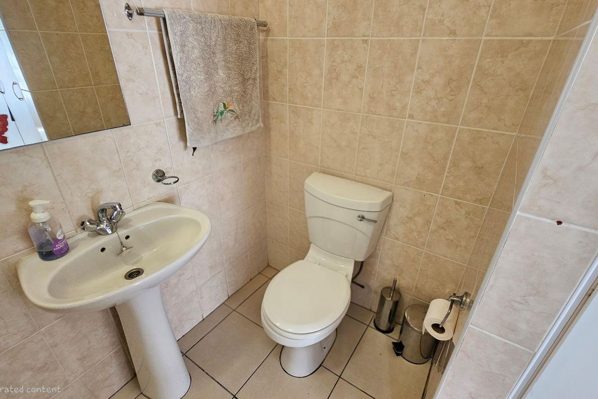 A compact guest bathroom featuring a pedestal basin, a standard toilet, and neutral wall and floor tiling.