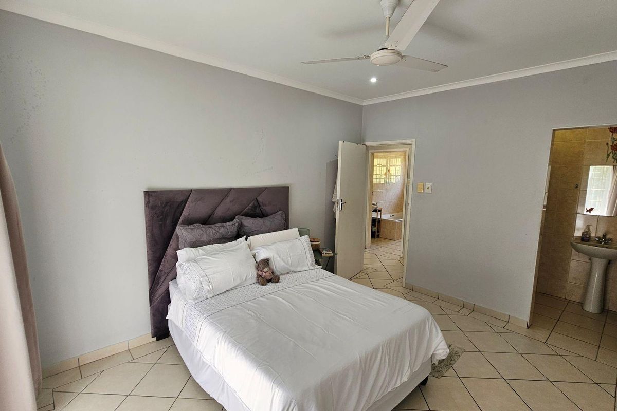 Spacious bedroom featuring tiled flooring, a ceiling fan, and an en-suite bathroom with a pedestal basin.