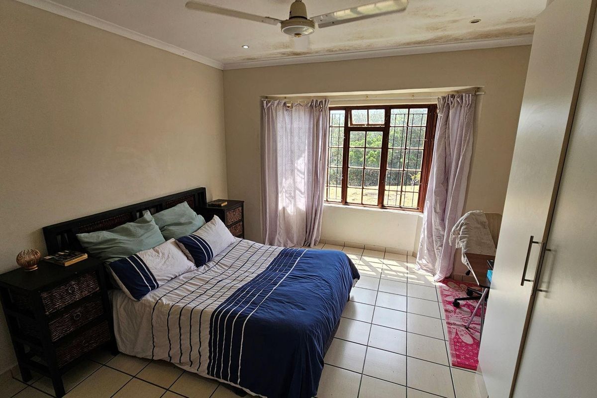A bedroom featuring tiled flooring, a ceiling fan, and a window with security bars, requiring some ceiling maintenance.