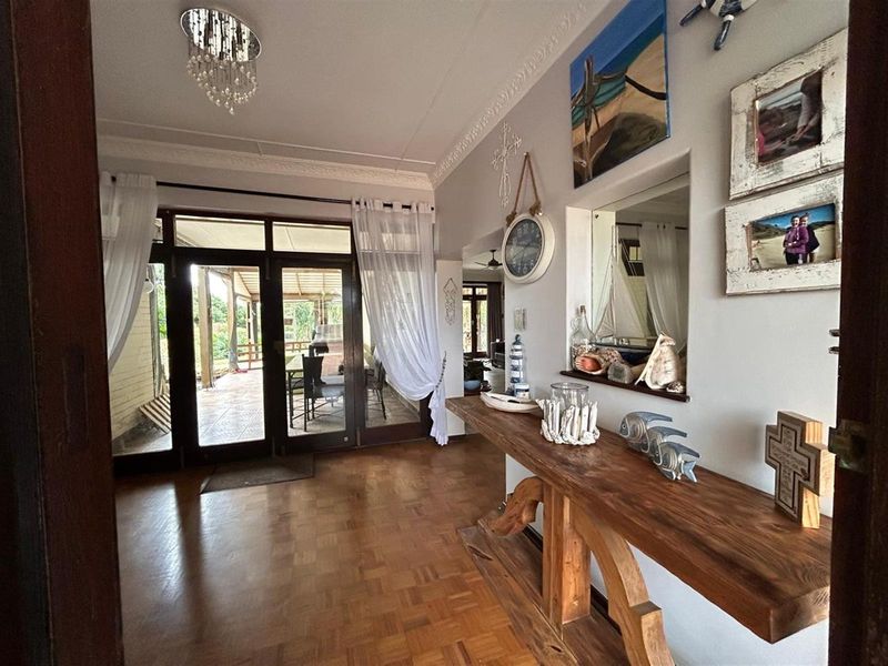 A bright entrance hall featuring polished parquet flooring, decorative ceiling cornices, and glass-paneled doors leading to an outdoor patio area.