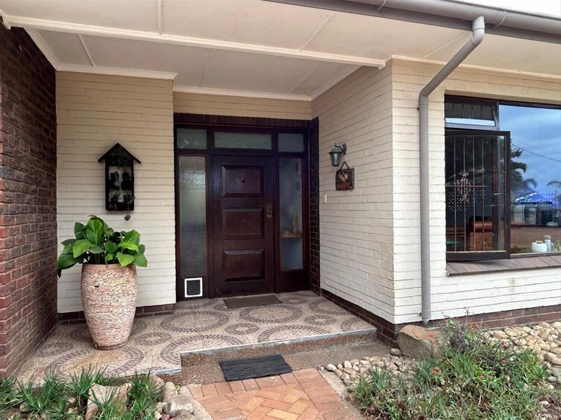 Covered front entrance featuring a solid timber door with side light panels, tiled porch area, and brick facade.