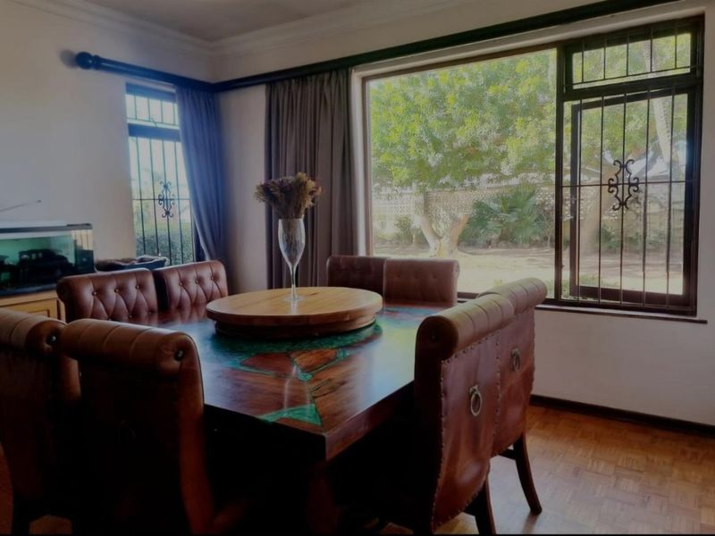 A dining room featuring parquet flooring, large windows with security bars, and crown molding, offering a view of the garden.