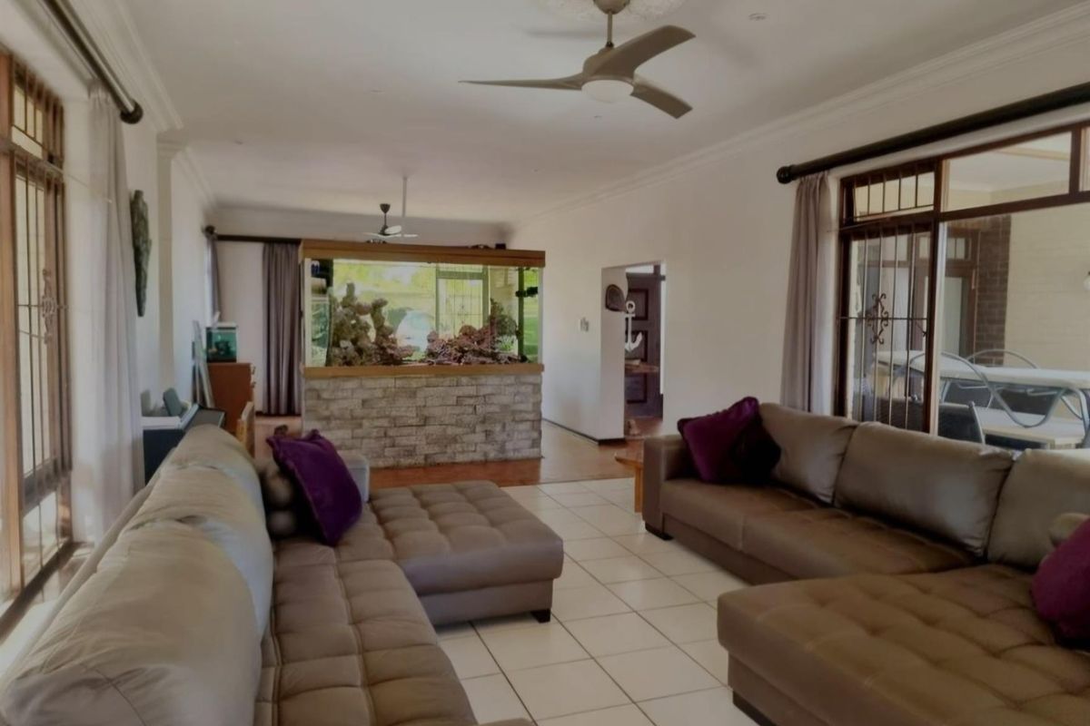 Spacious living area featuring tiled flooring, ceiling fans, and a built-in stone-clad aquarium partition, offering a bright and open layout.