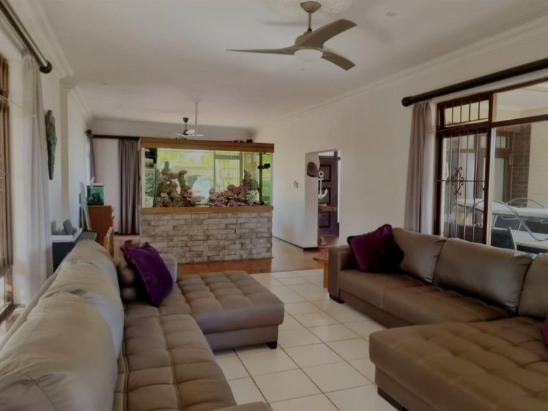 Spacious living area featuring tiled flooring, ceiling fans, and a built-in stone-clad aquarium partition, offering a bright and open layout.