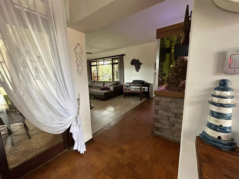 An inviting entrance hallway featuring parquet flooring, leading into an open-plan living area with tiled floors and a built-in stone-clad feature wall.