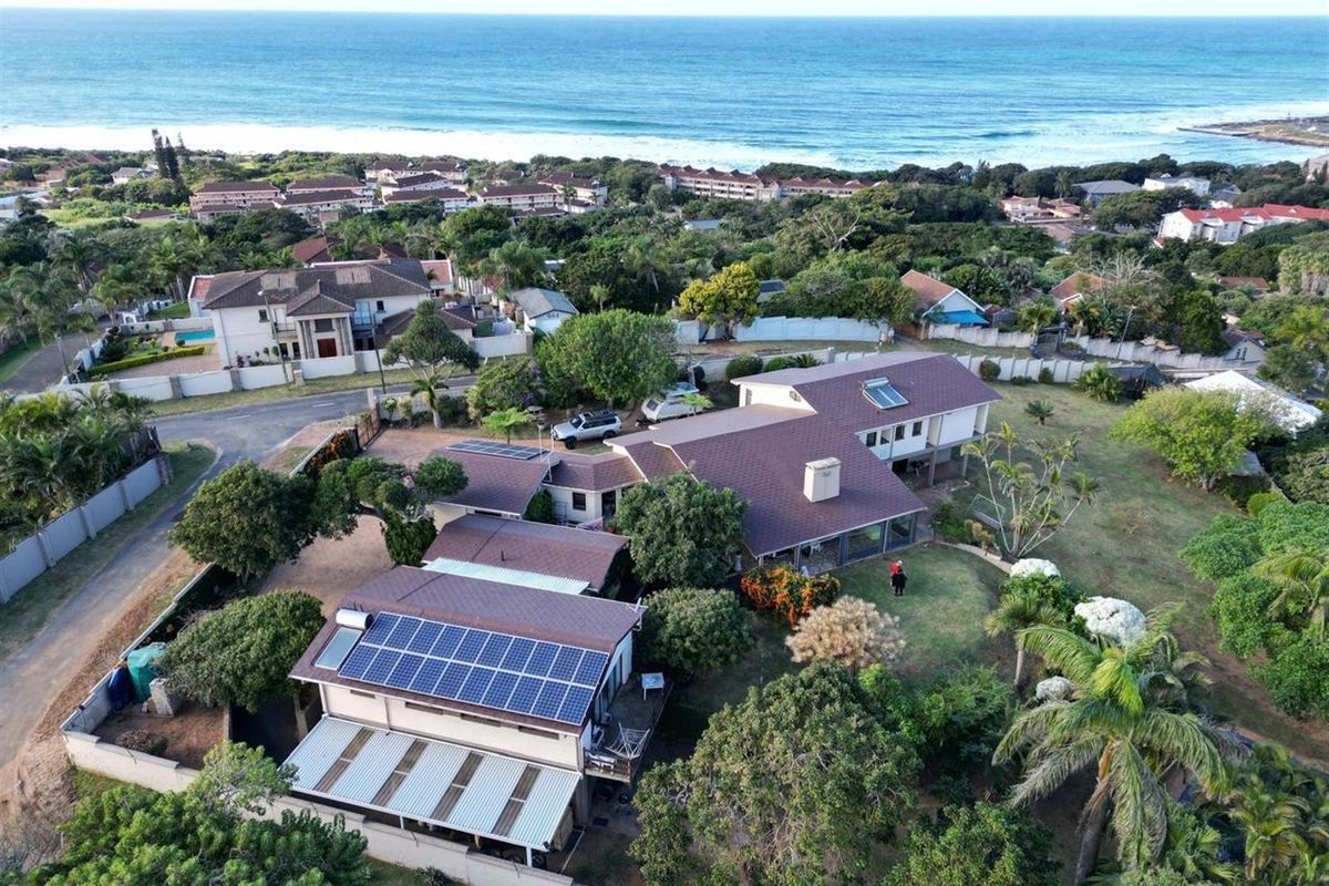 Aerial view of a coastal residential property featuring a large roof with solar panels, expansive garden, and proximity to the ocean.