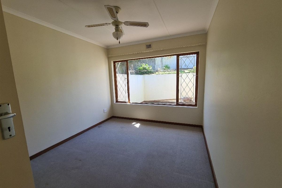 A vacant bedroom featuring neutral walls, a ceiling fan, and a large window with security bars overlooking an exterior wall.
