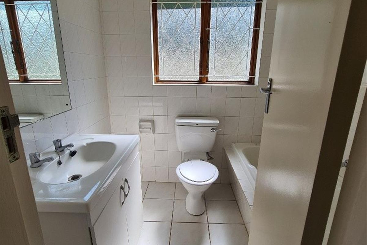A functional bathroom featuring a vanity basin, toilet, and built-in bathtub with white tiled walls and flooring.
