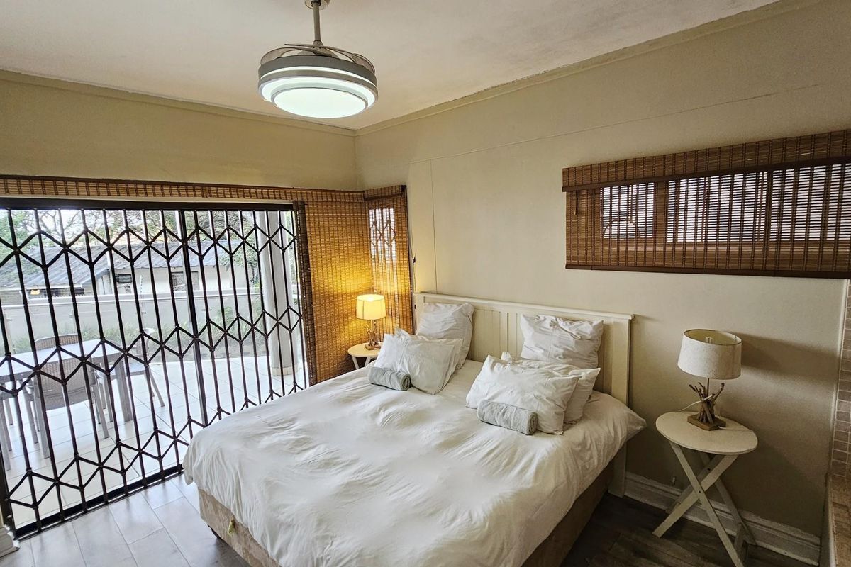 A bedroom featuring tiled flooring, a ceiling fan, and sliding security gates providing direct access to an outdoor patio area.