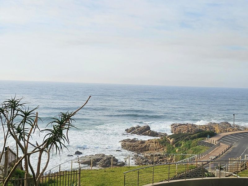 A scenic coastal view overlooking the ocean, rocky shoreline, and a nearby coastal road, showcasing the property's prime seaside location.