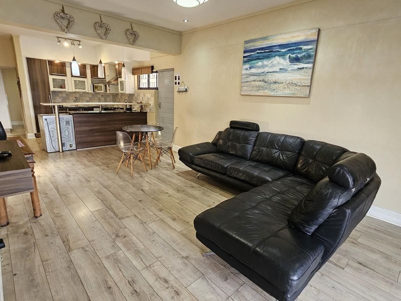 Open-plan living and kitchen area featuring wood-look laminate flooring, a breakfast bar, and integrated cabinetry, creating a functional and connected living space.