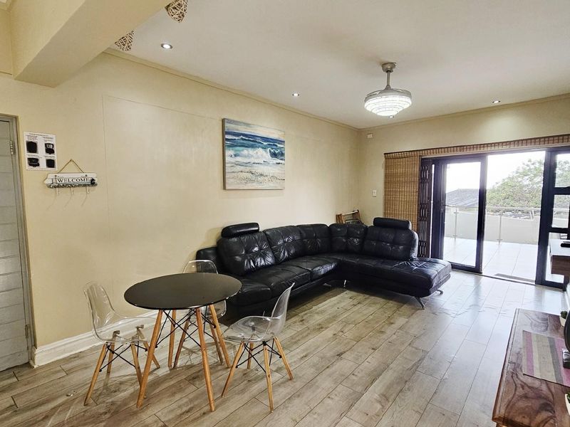Spacious living area featuring wood-look flooring, recessed ceiling lighting, and large sliding glass doors providing access to an outdoor balcony.