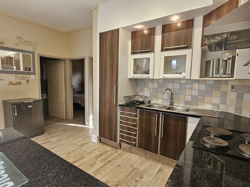 A functional kitchen featuring dark wood-look cabinetry, granite countertops, a built-in hob, and an extractor fan, with adjacent access to interior rooms.