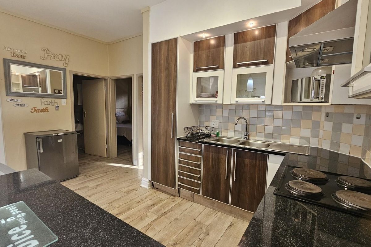 A functional kitchen featuring dark wood-look cabinetry, granite countertops, a built-in hob, and an extractor fan, with adjacent access to interior rooms.