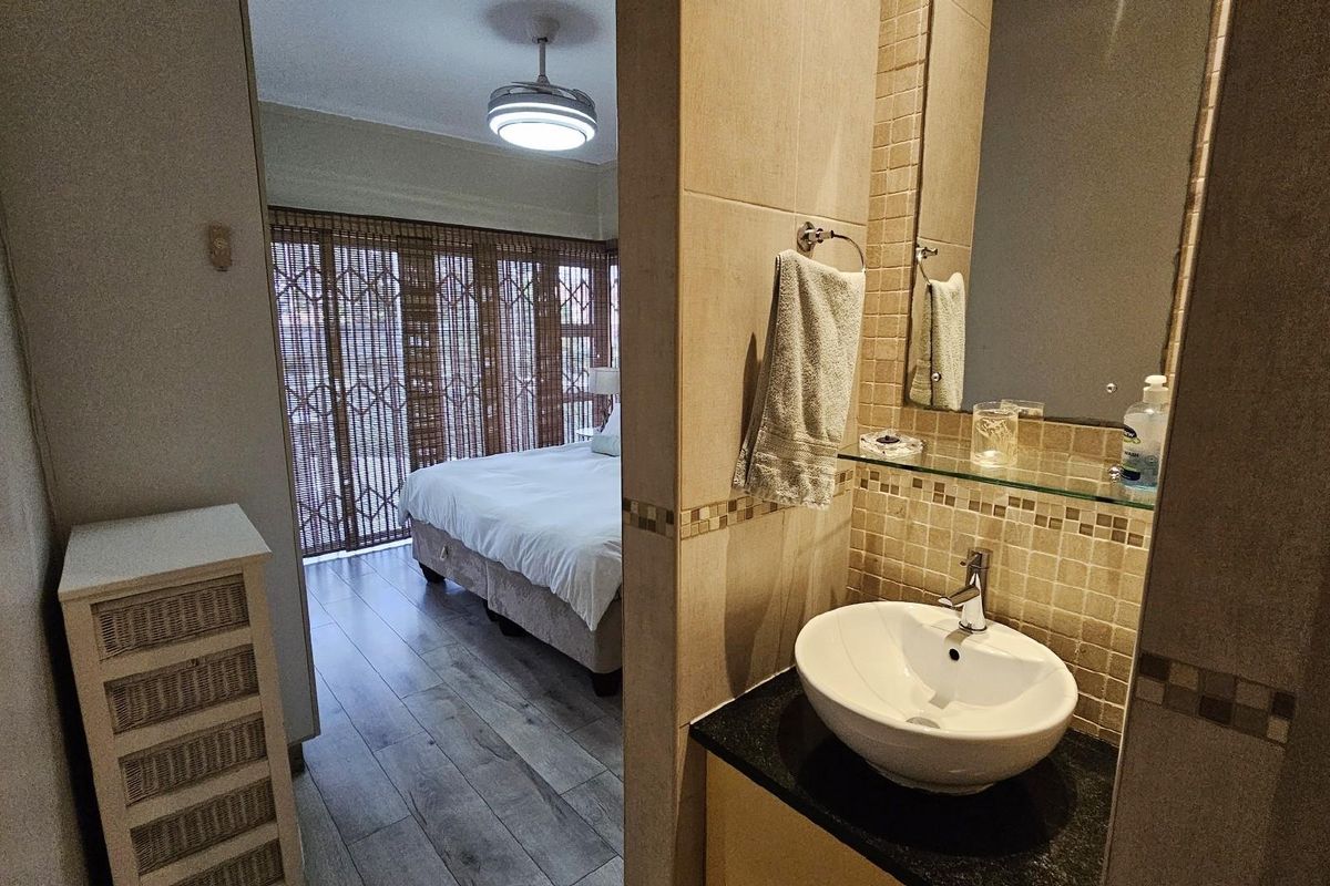 A view from a bathroom vanity area looking into an adjacent bedroom with wood-look flooring and sliding security gates.