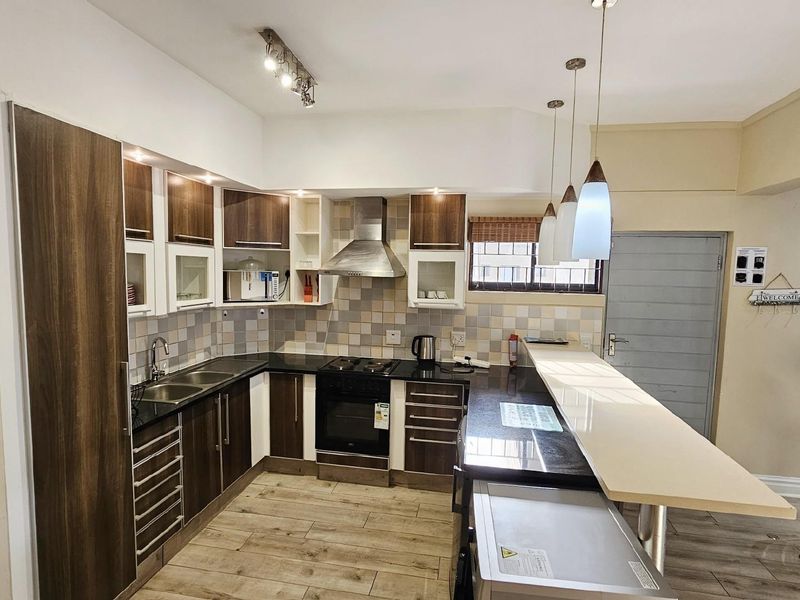 Modern kitchen featuring dark wood cabinetry, granite countertops, a breakfast bar, stainless steel extractor fan, and tiled backsplash.