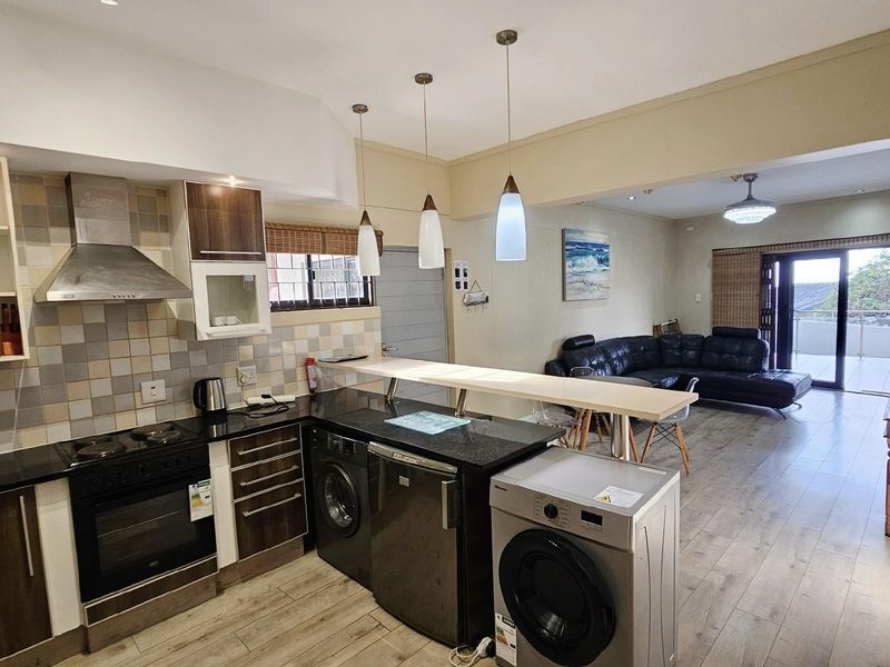 Open-plan kitchen and living area featuring dark cabinetry, granite countertops, integrated appliances, and direct access to a balcony.