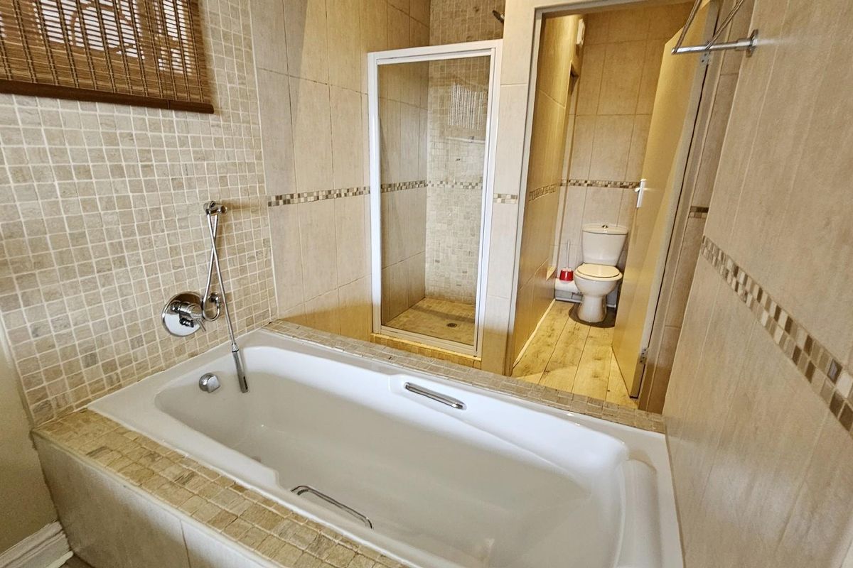 A functional bathroom featuring a built-in bathtub, a separate glass-enclosed shower, and a private toilet area with neutral wall and floor tiling.