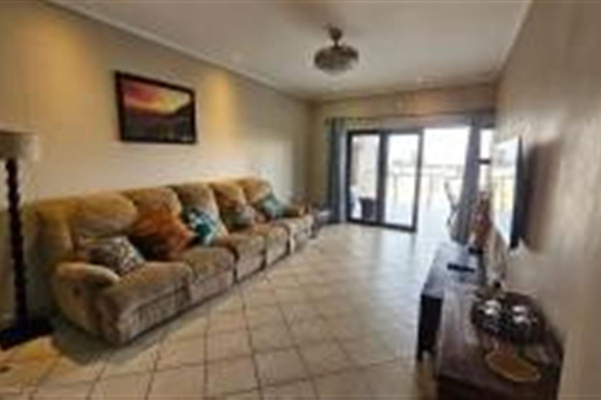 A spacious living room featuring tiled flooring, recessed ceiling lighting, and sliding glass doors that provide access to an outdoor balcony area.