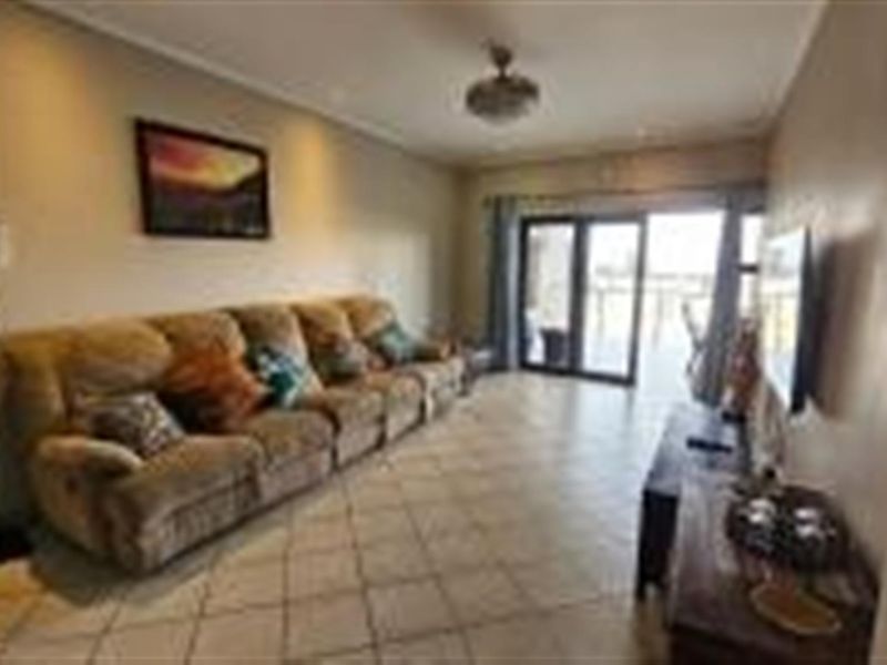 A spacious living room featuring tiled flooring, recessed ceiling lighting, and sliding glass doors that provide access to an outdoor balcony area.