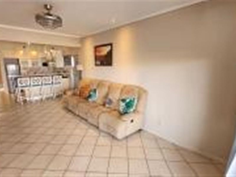 An open-plan living and kitchen area featuring tiled flooring, a ceiling fan, and a breakfast bar counter.