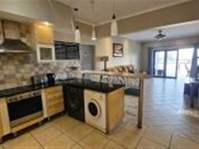 Open-plan kitchen featuring built-in cabinetry, stainless steel extractor fan, and integrated appliances, flowing into a spacious living area with access to a balcony.