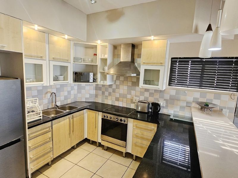 A functional kitchen featuring light wood cabinetry, black granite countertops, a built-in oven, hob, and stainless steel extractor fan with tiled splashbacks.