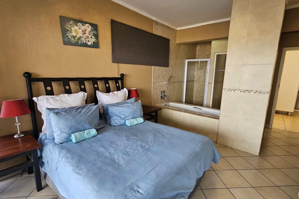 Open-plan bedroom featuring an integrated en-suite bathroom with a built-in bathtub and shower enclosure, finished with tiled flooring throughout.