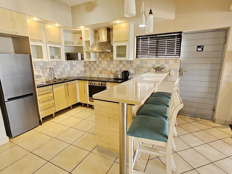 A functional kitchen featuring light wood cabinetry, a breakfast bar, tiled backsplash, and integrated stainless steel appliances, including a built-in oven and extractor fan.