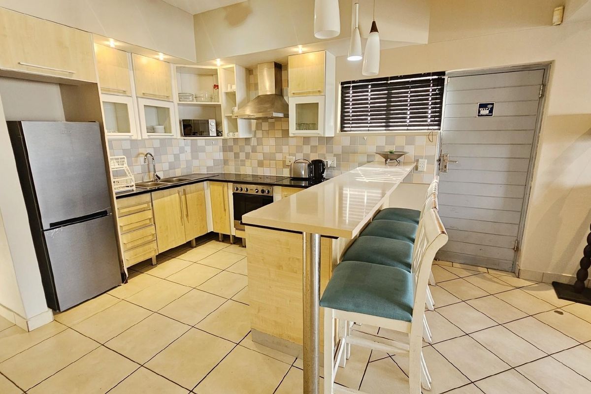 A functional kitchen featuring light wood cabinetry, a breakfast bar, tiled backsplash, and integrated stainless steel appliances, including a built-in oven and extractor fan.