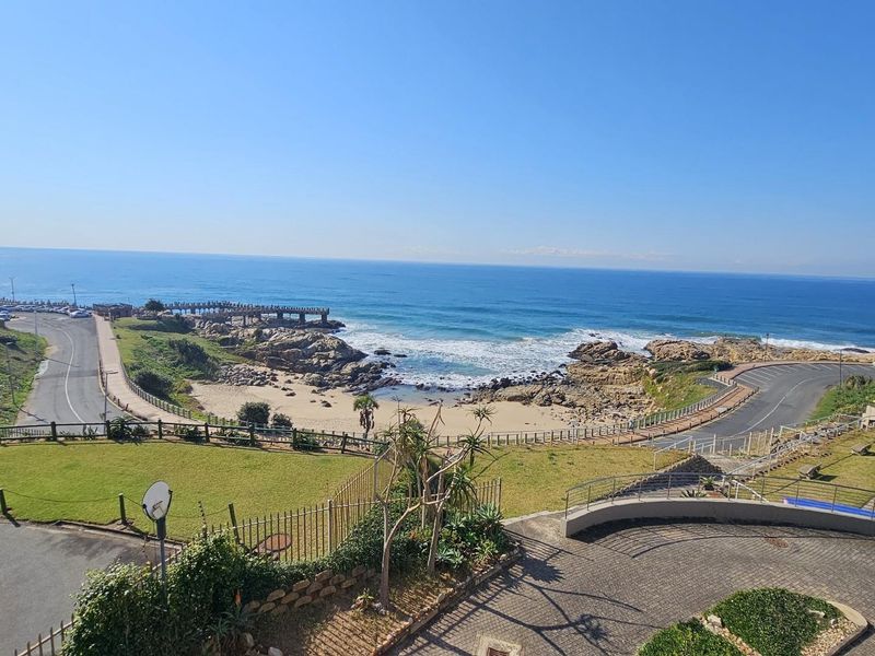 A scenic elevated view overlooking the coastline, featuring a sandy beach, rocky outcrops, and surrounding coastal infrastructure.