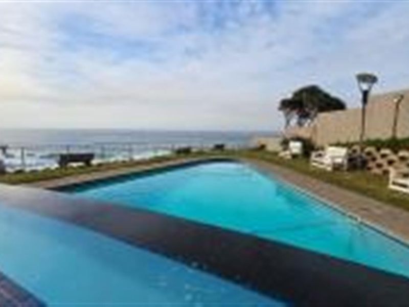 A communal swimming pool area featuring a paved surround, landscaped lawn, and expansive ocean views.
